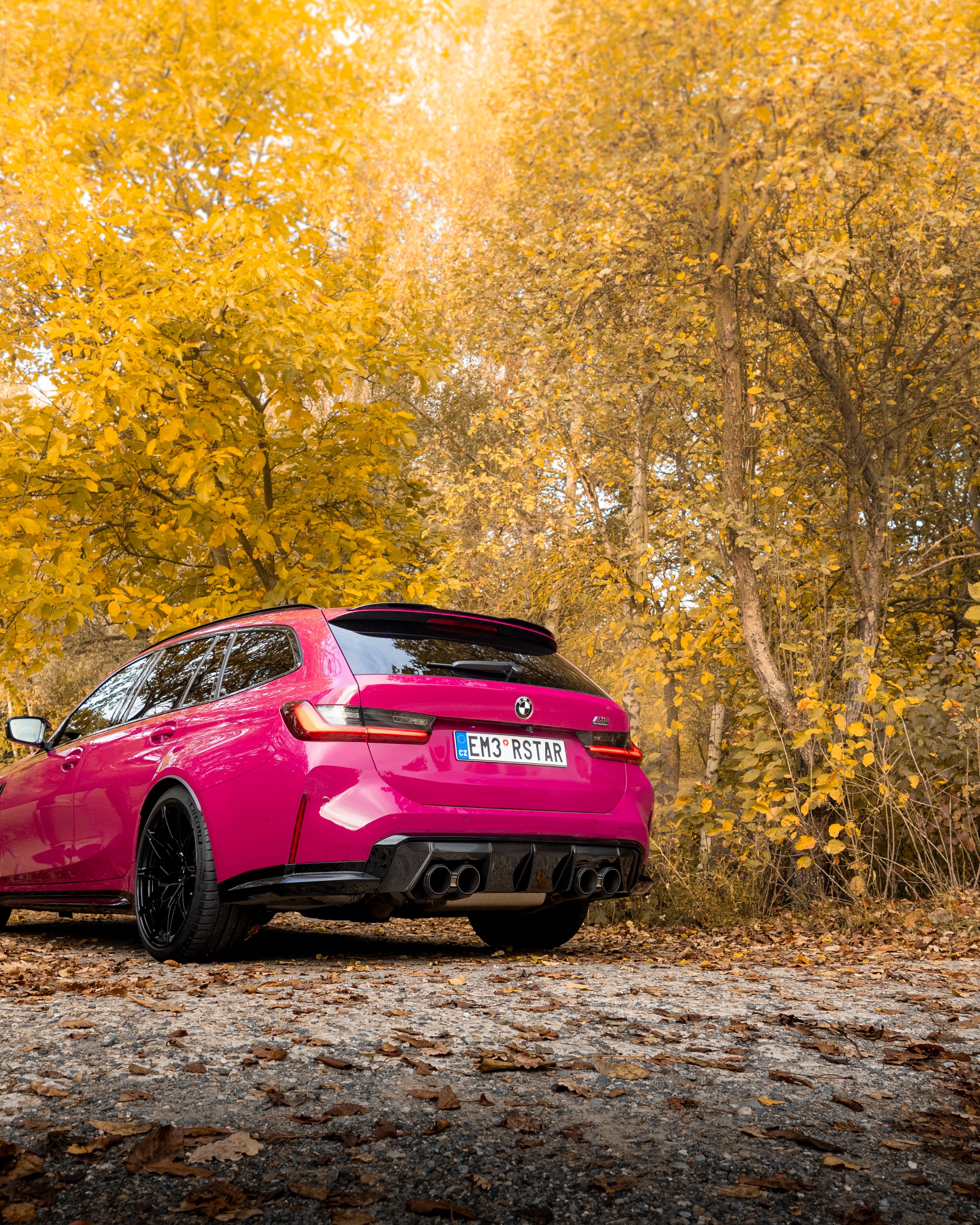 BMW M3 G91 Ruby Star parked in autumn forest with golden leaves